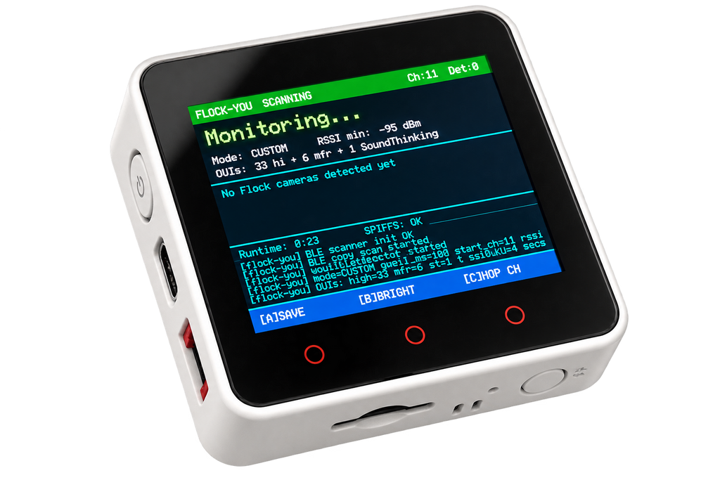 A white handheld electronic device with a black front face and a colorful LCD screen, shown on a plain white background. The screen displays a blue and green interface with text including 'FLOCK-YOU SCANNING' and 'Monitoring.